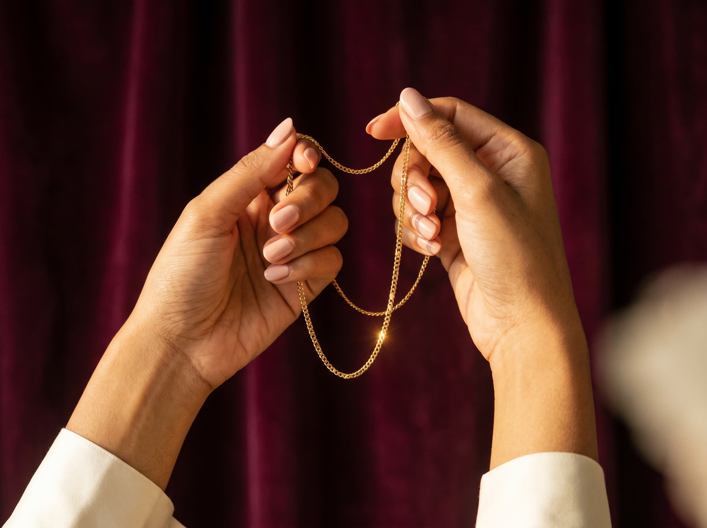 Hands inspecting a gold chain in golden window light
